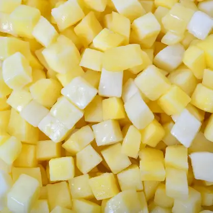 A top-down, close-up view of a large pile of raw, evenly diced yellow and white potato cubes
