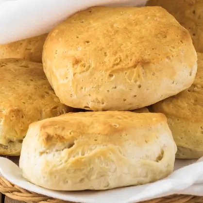 A close-up view of several thick, golden-brown baked biscuits stacked together in a lined basket