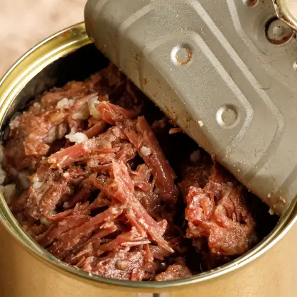 A close-up of a partially opened tin can filled with packed, shredded preserved meat