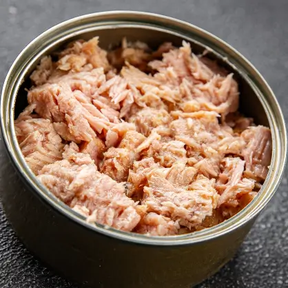 A close-up of an opened round tin can filled with flaked light tuna