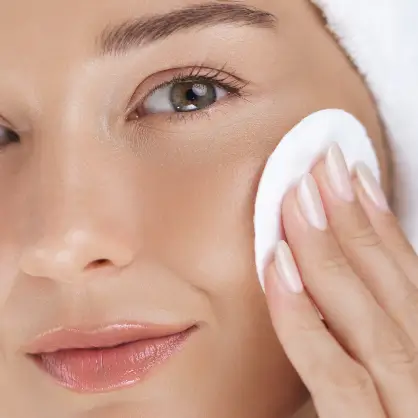 A close-up of a person's face holding a round white cotton pad against their cheek