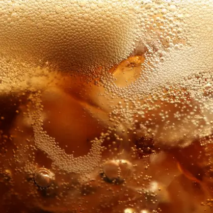 A macro close-up of bubbly, carbonated brown soda in a glass