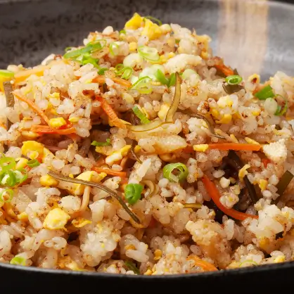 A close-up view of fried rice mixed with egg, carrots, and green onions in a dark pan