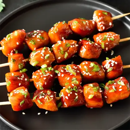 Skewers of glossy, glazed meat chunks sprinkled with sesame seeds and green onions
