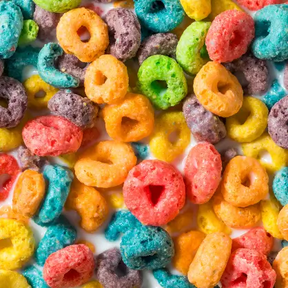 A vibrant, close-up overhead shot of colorful, ring-shaped breakfast cereal pieces in shades of pink, yellow, orange, green, blue, and purple