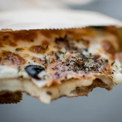 Close-up of a pizza slice partially sliding out of a white paper bag