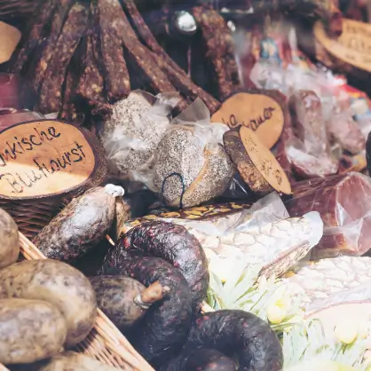 A rustic display of various cured meats and sausages with small wooden label tags