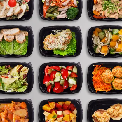 A top-down view of multiple black plastic takeout containers arranged in a grid, filled with different salads, vegetables, and prepared meals