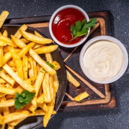 Plate of fries next to bowls of ketchup and mayonnaise