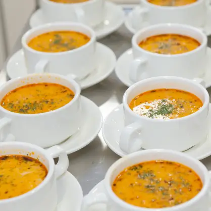 A high-angle view of multiple small white cups on saucers filled with an orange, creamy soup garnished with green herbs