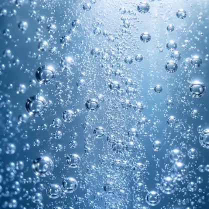 A close-up, macro view of numerous small air bubbles suspended and rising in blue sparkling water