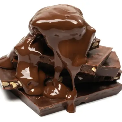 Thick, glossy melted chocolate being poured over a stack of broken dark chocolate squares against a white background
