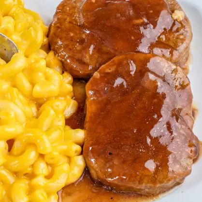 A close-up of a plated meal featuring two meat patties smothered in brown gravy, served next to a portion of macaroni and cheese