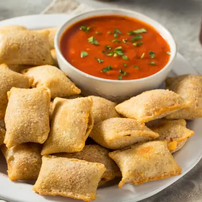 A white plate filled with baked pizza rolls surrounding a small bowl of red marinara dipping sauce garnished with green herbs