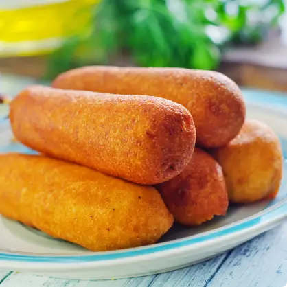 A stack of cooked corn dogs piled on a light blue plate