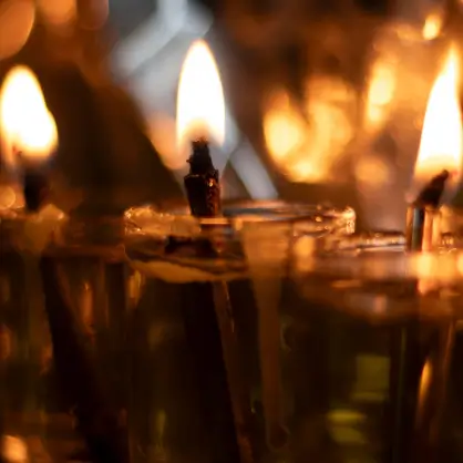A close-up of multiple small glass oil lamps with lit wicks glowing warmly in the dark