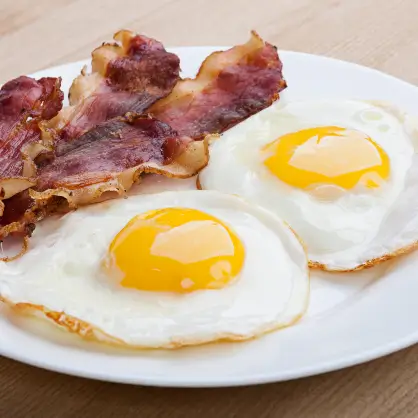 A white plate serving two sunny-side-up fried eggs next to several strips of cooked, crispy bacon